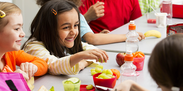 Kids smiling and eating a healthy lunch.